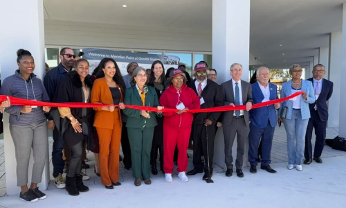 Folks standing in front of Meridian Point holding red ribbon for Ribbon Cutting Ceremony